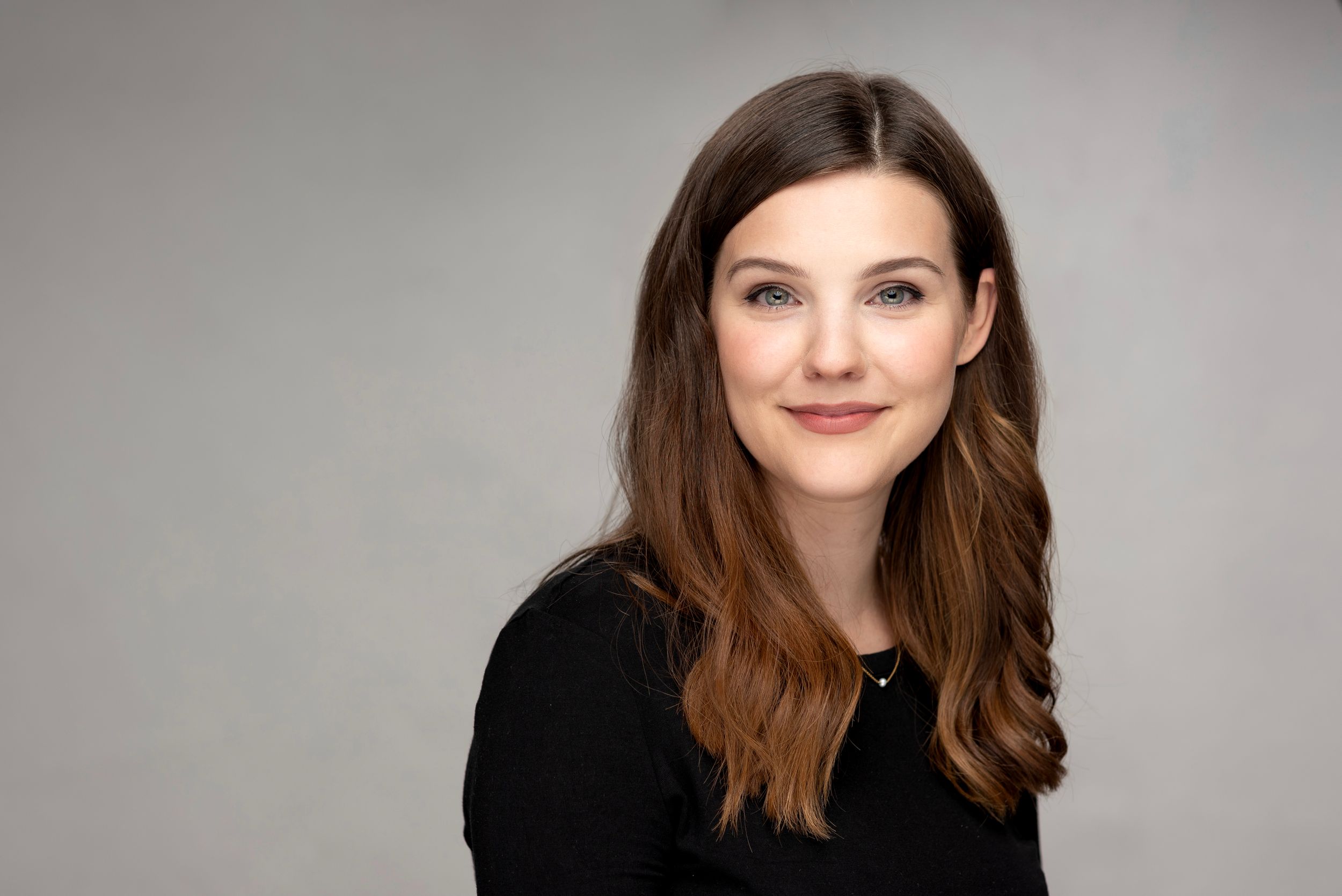 Professional studio headshot of someone wearing a black sweater against a light gray background.