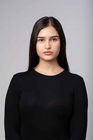 Portrait photo of someone with long dark hair wearing a simple black long-sleeved top against a gray background.