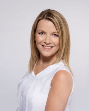 Professional portrait of person in white sleeveless top smiling against light background.