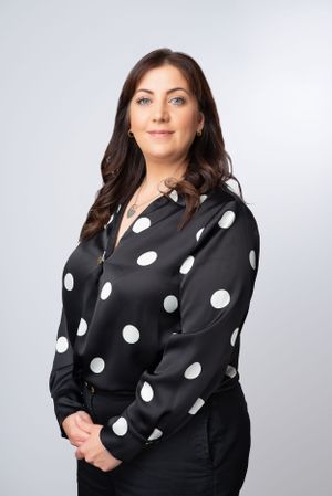 Professional portrait against gray background wearing a black and white polka dot blouse with long dark hair.