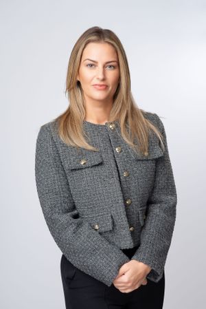 Professional portrait of someone wearing a gray textured tweed jacket with patch pockets against a light gray background.