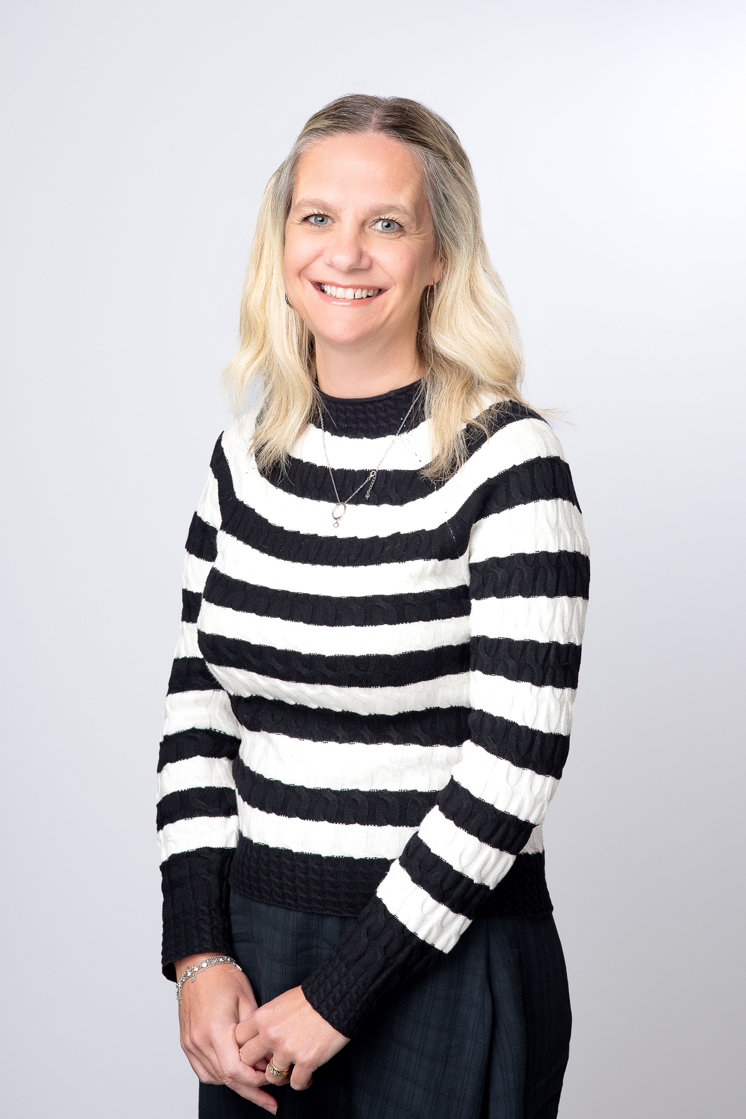 Professional portrait against gray background showing person wearing black and white striped knit sweater.
