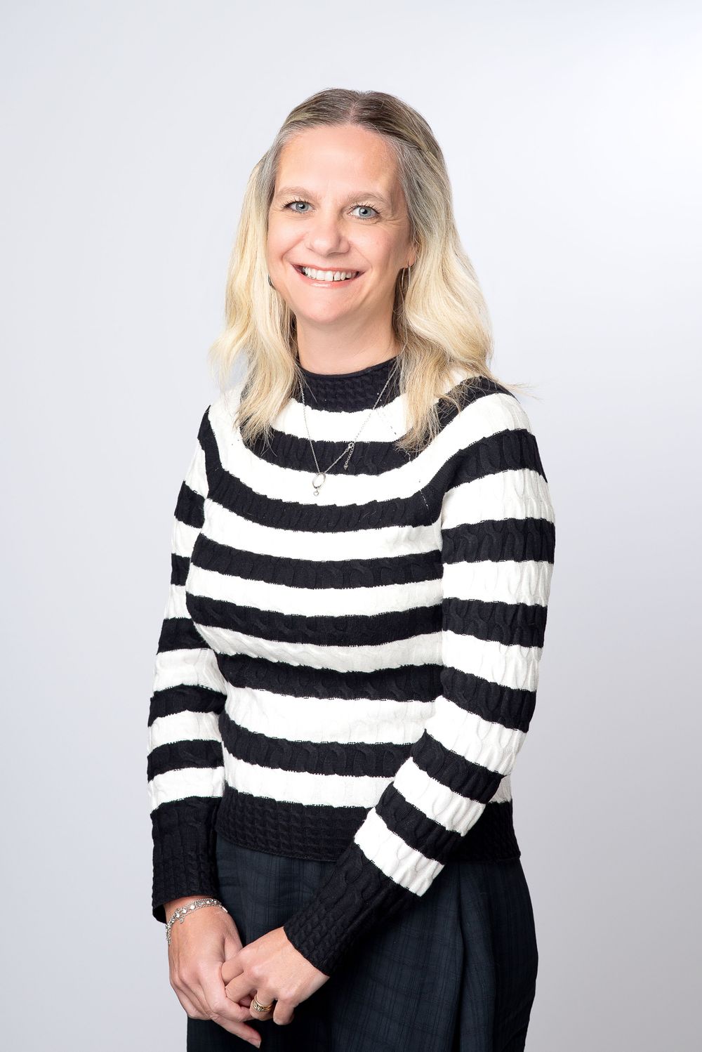 Professional portrait against gray background showing person wearing black and white striped knit sweater.