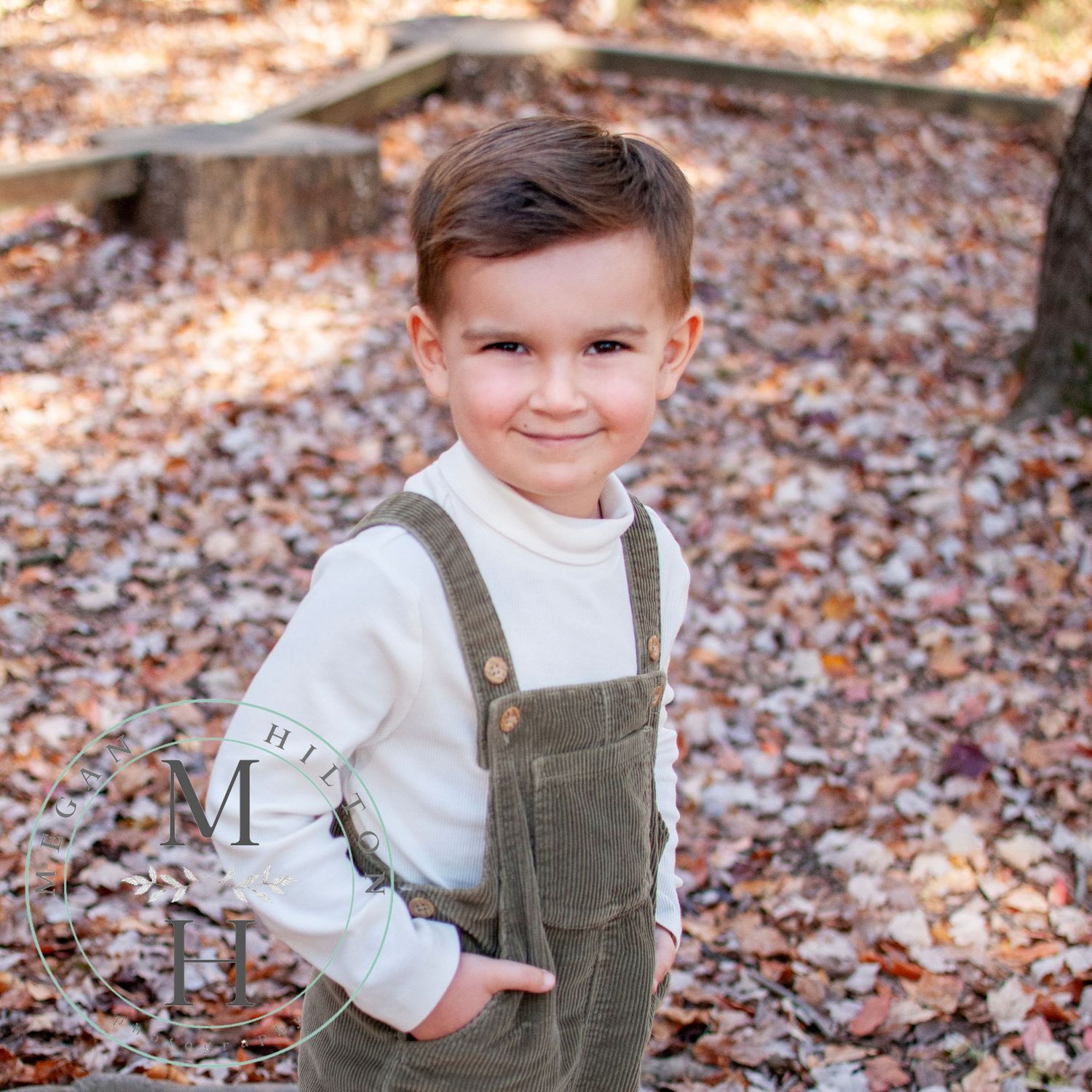 Toddler boy with overalls standing in fall leaves