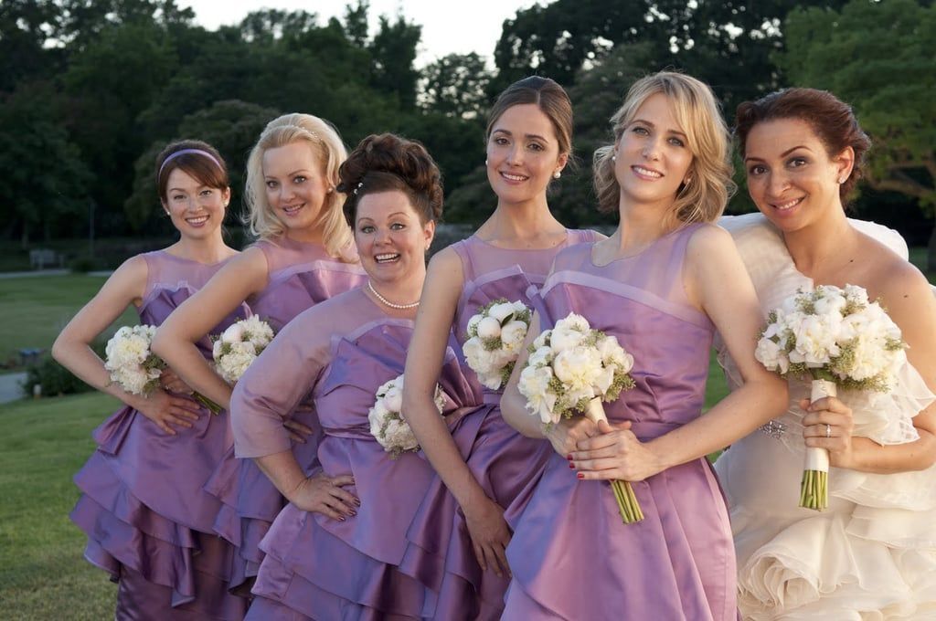 Wedding party in purple bridesmaid dresses holding white bouquets outdoors.