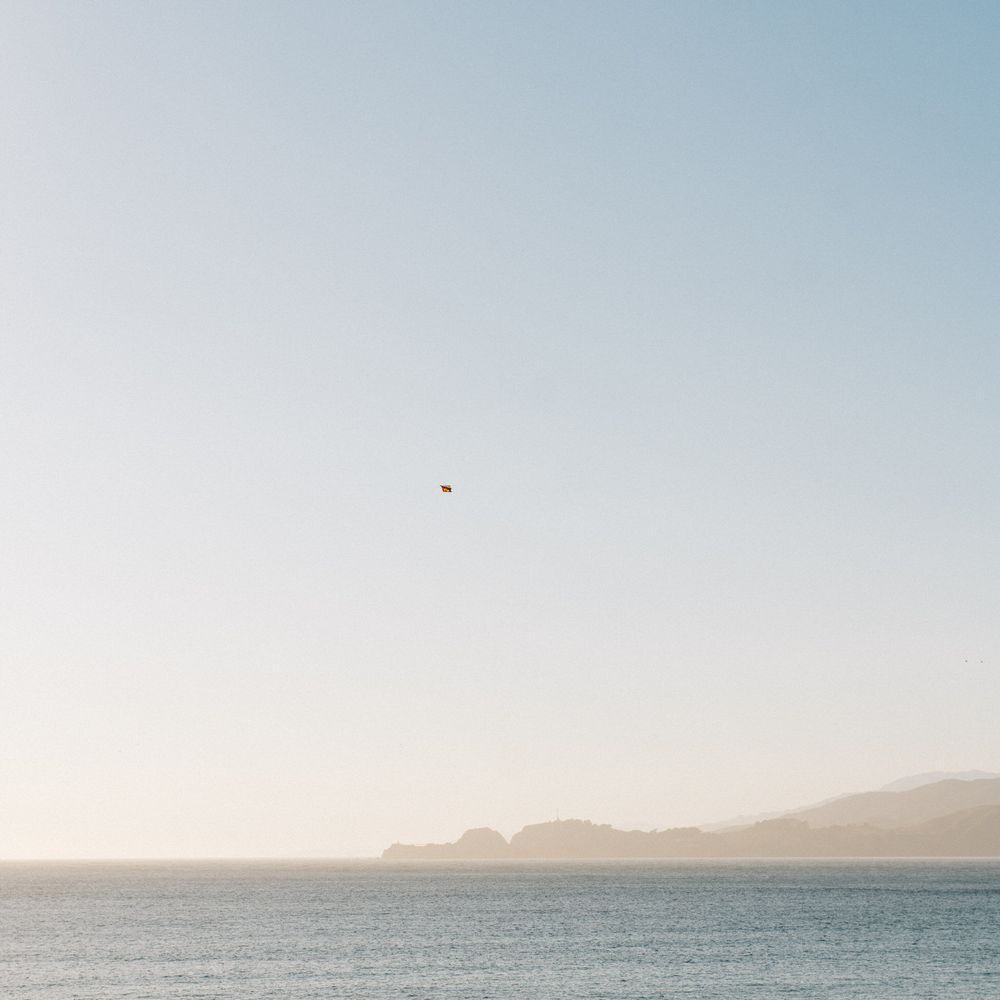 Minimalist seascape with single bird flying over ocean against distant mountains.