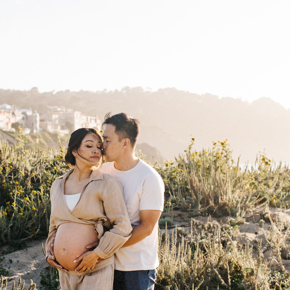 Intimate maternity photoshoot on coastal cliff during sunset.