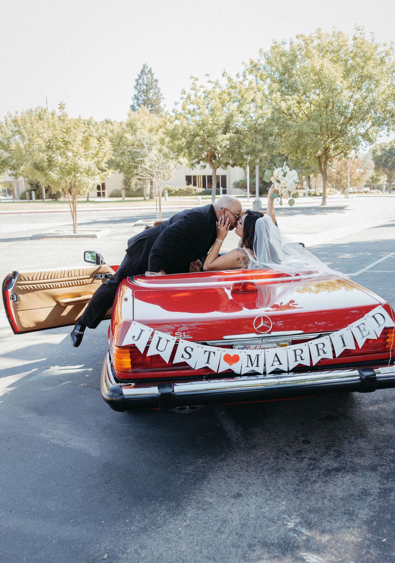 Red vintage convertible with Just Married banner parked in sunny parking lot.