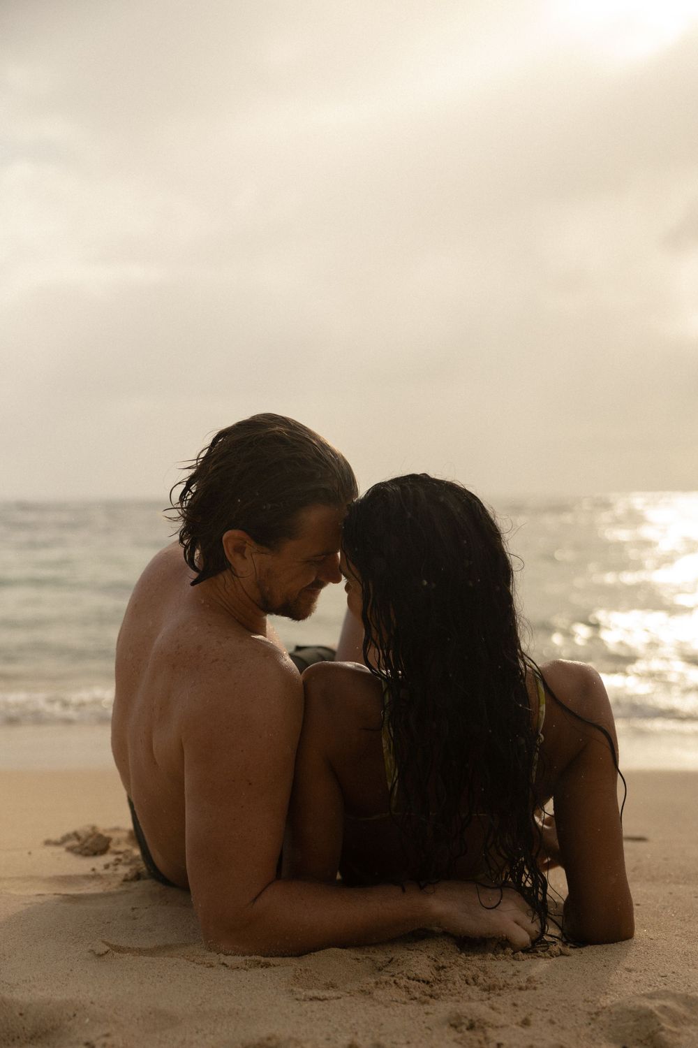 Two people sharing an intimate moment while sitting on the beach at sunset.