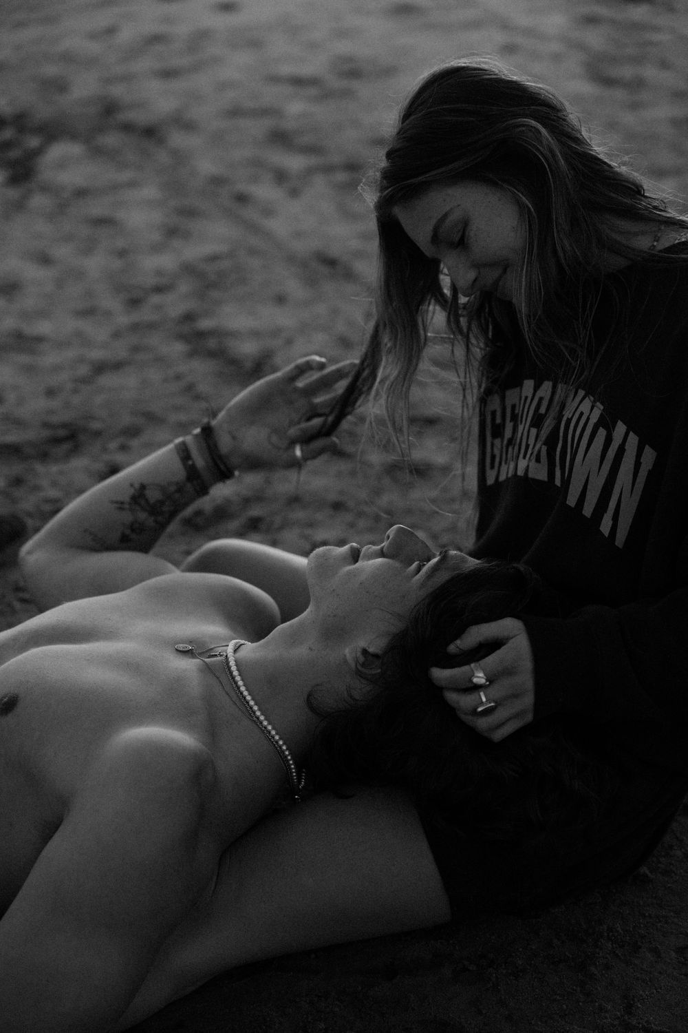 Intimate black and white beach scene of two people sharing a tender moment on the sand.