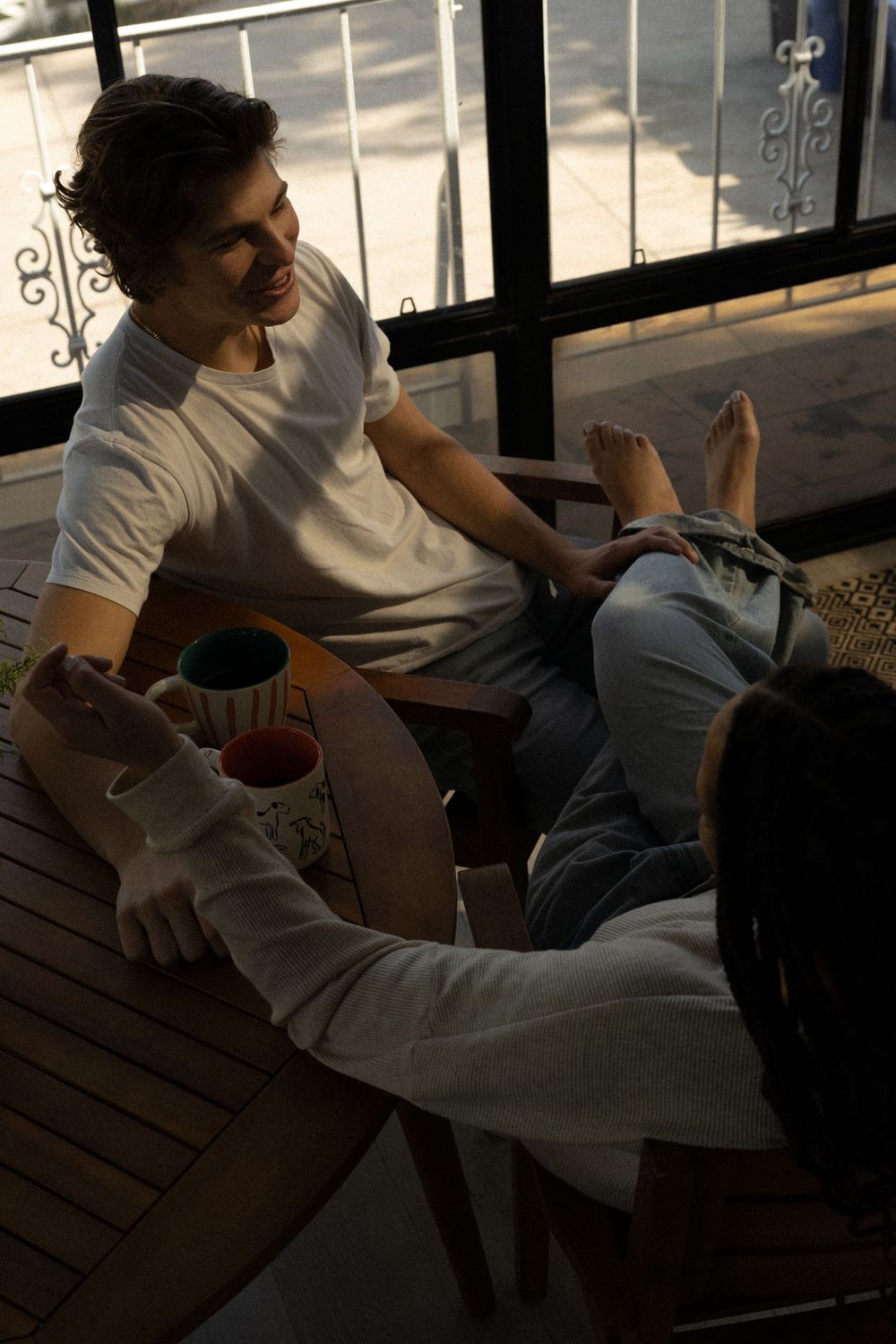 Relaxed balcony scene with two people enjoying drinks in warm afternoon light.