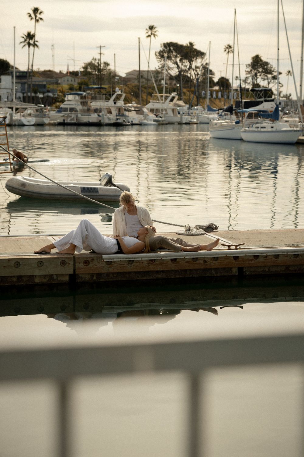 Person relaxing on dock with boats and palm trees in marina background.