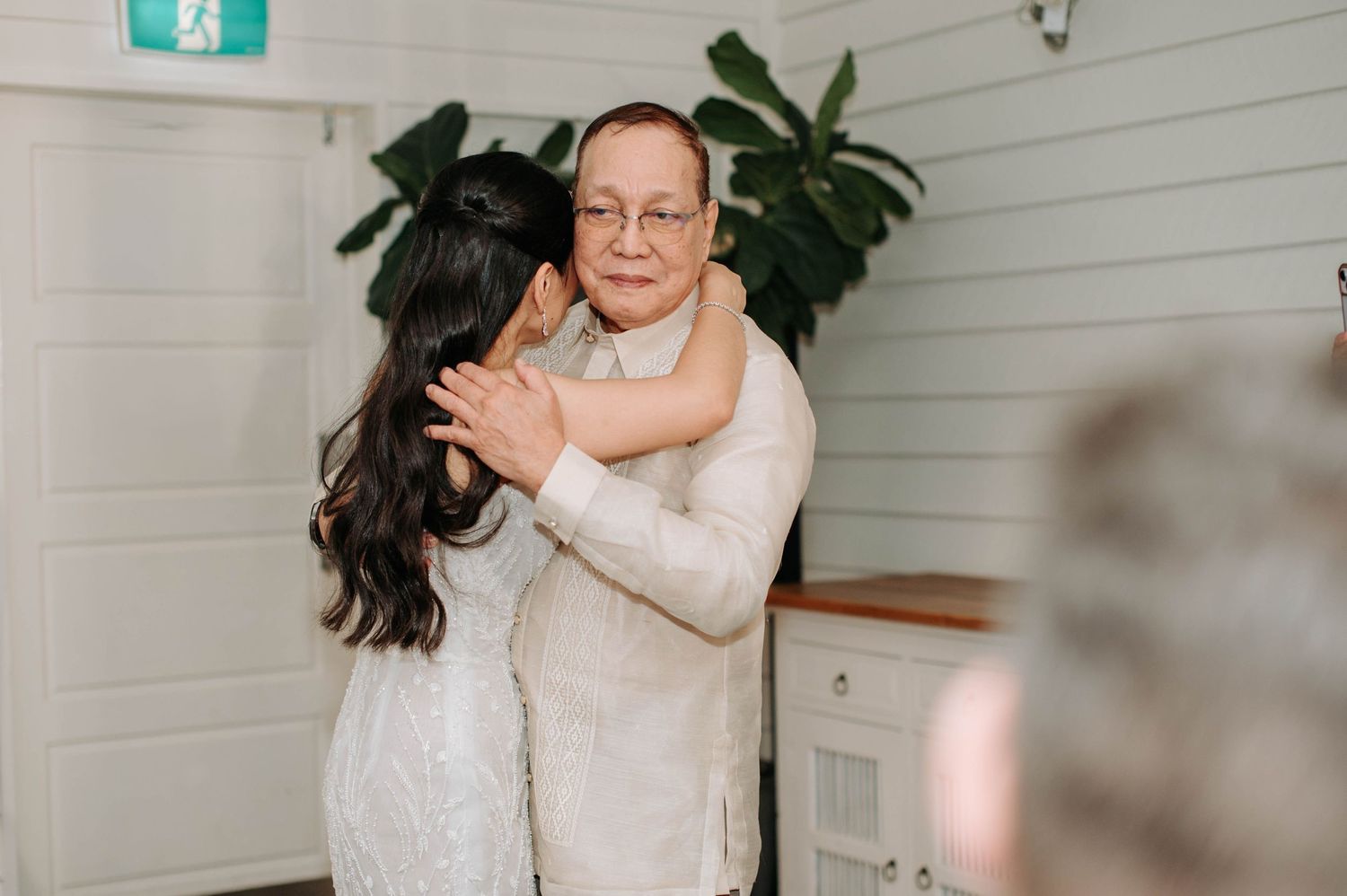A wedding couple dancing closely together in a white interior space with plants.