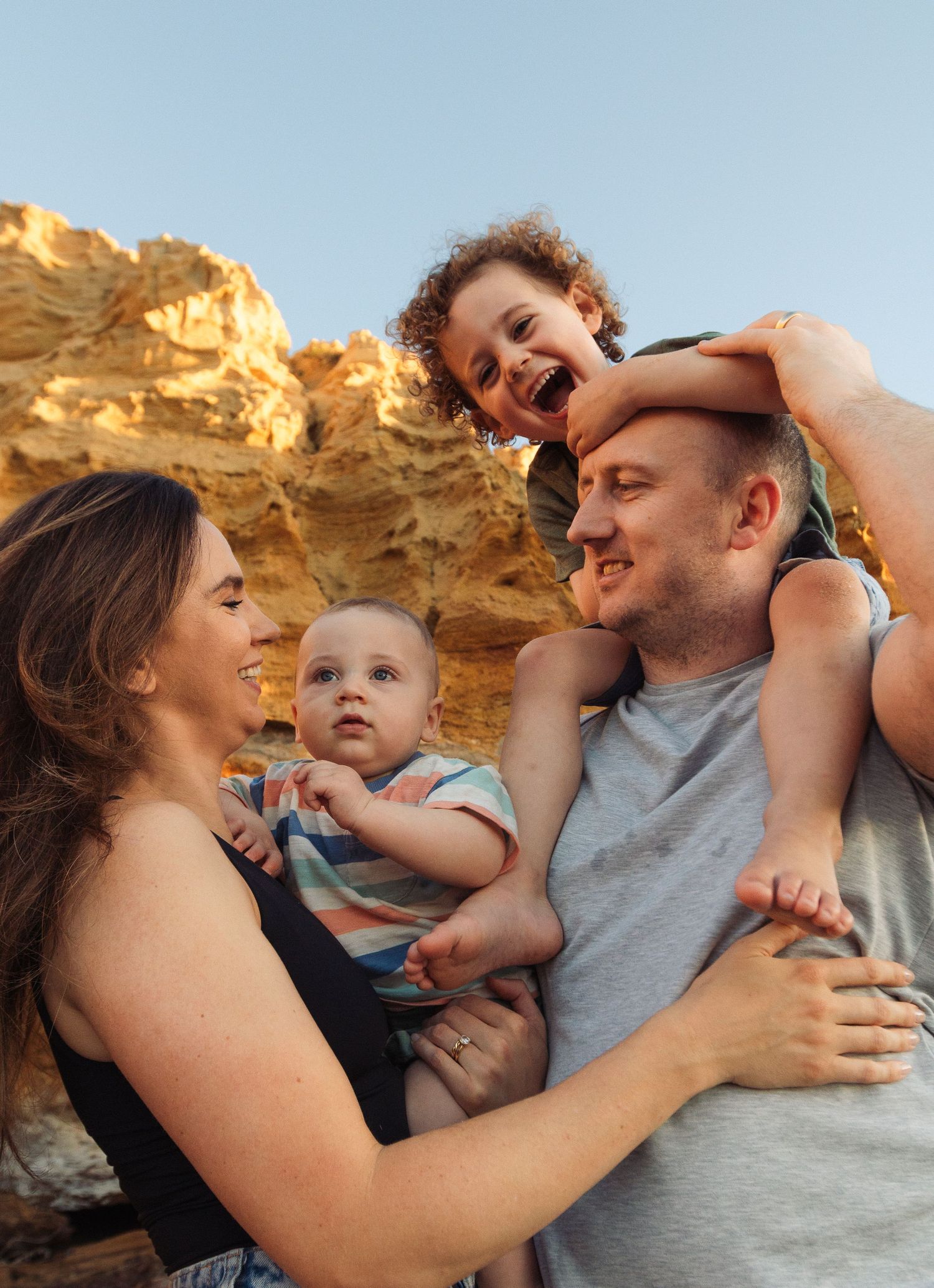 A happy family enjoys a tender moment together against golden rock formations during sunset.