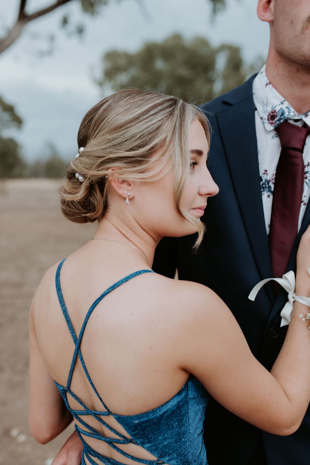 Formal couple embracing in evening wear against rural backdrop.