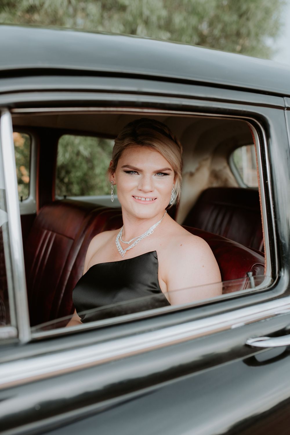 Classic car interior showing passenger in formal attire and necklace.