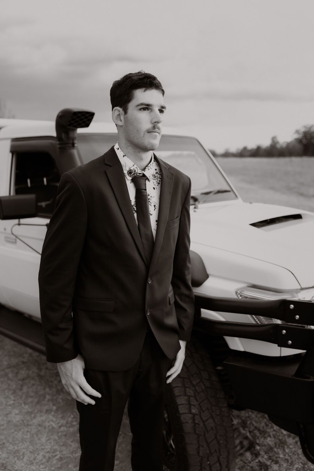 Well-dressed person standing next to classic white car at dusk.