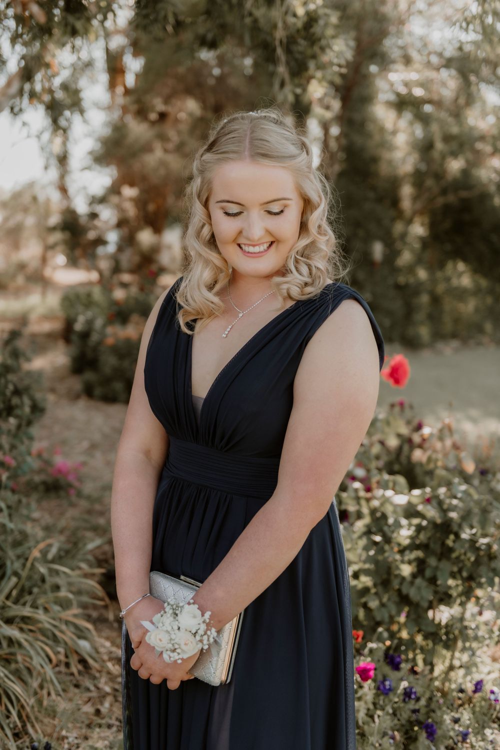 Formal portrait in a navy blue dress with blonde curls standing in a garden setting with flowers.