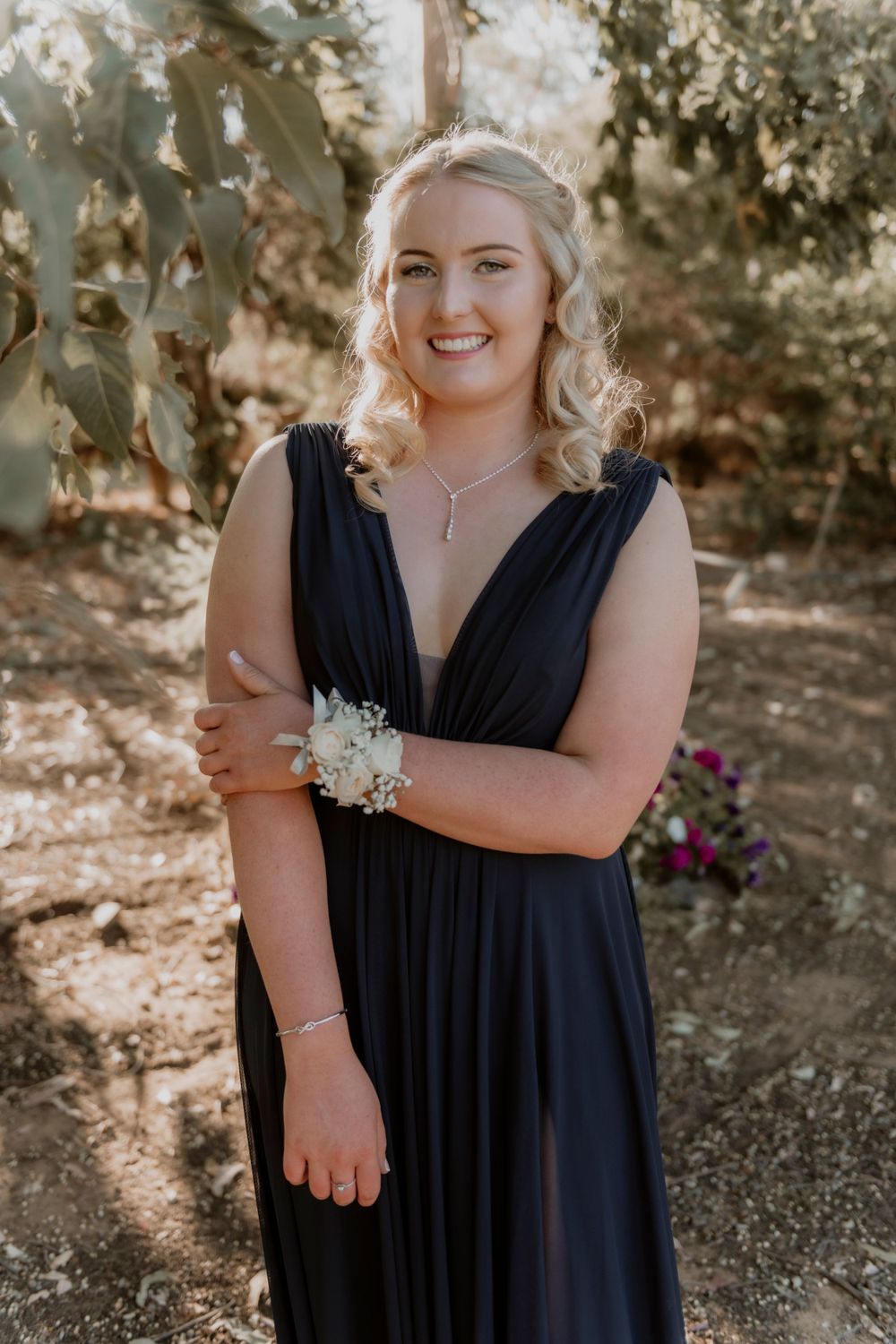 Elegant formal attire with a navy v-neck dress and delicate wrist corsage in an outdoor garden.