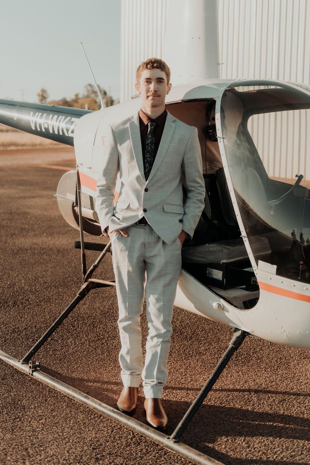 Person in light gray suit standing beside small aircraft on tarmac.