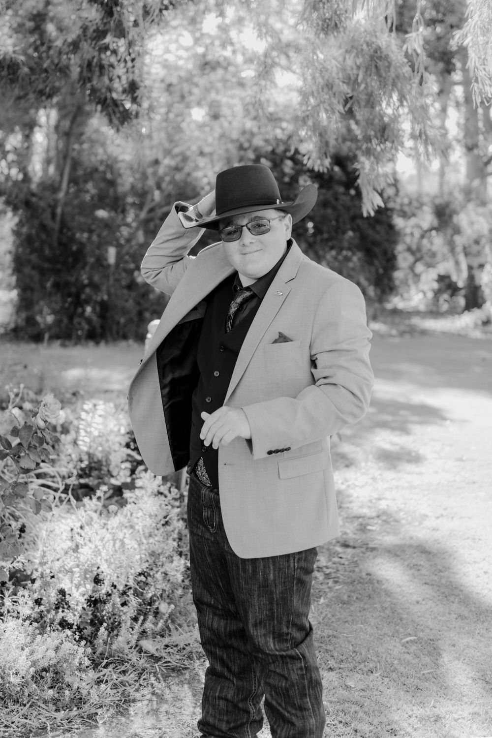 Black and white portrait of someone in a light suit and hat tipping the brim.