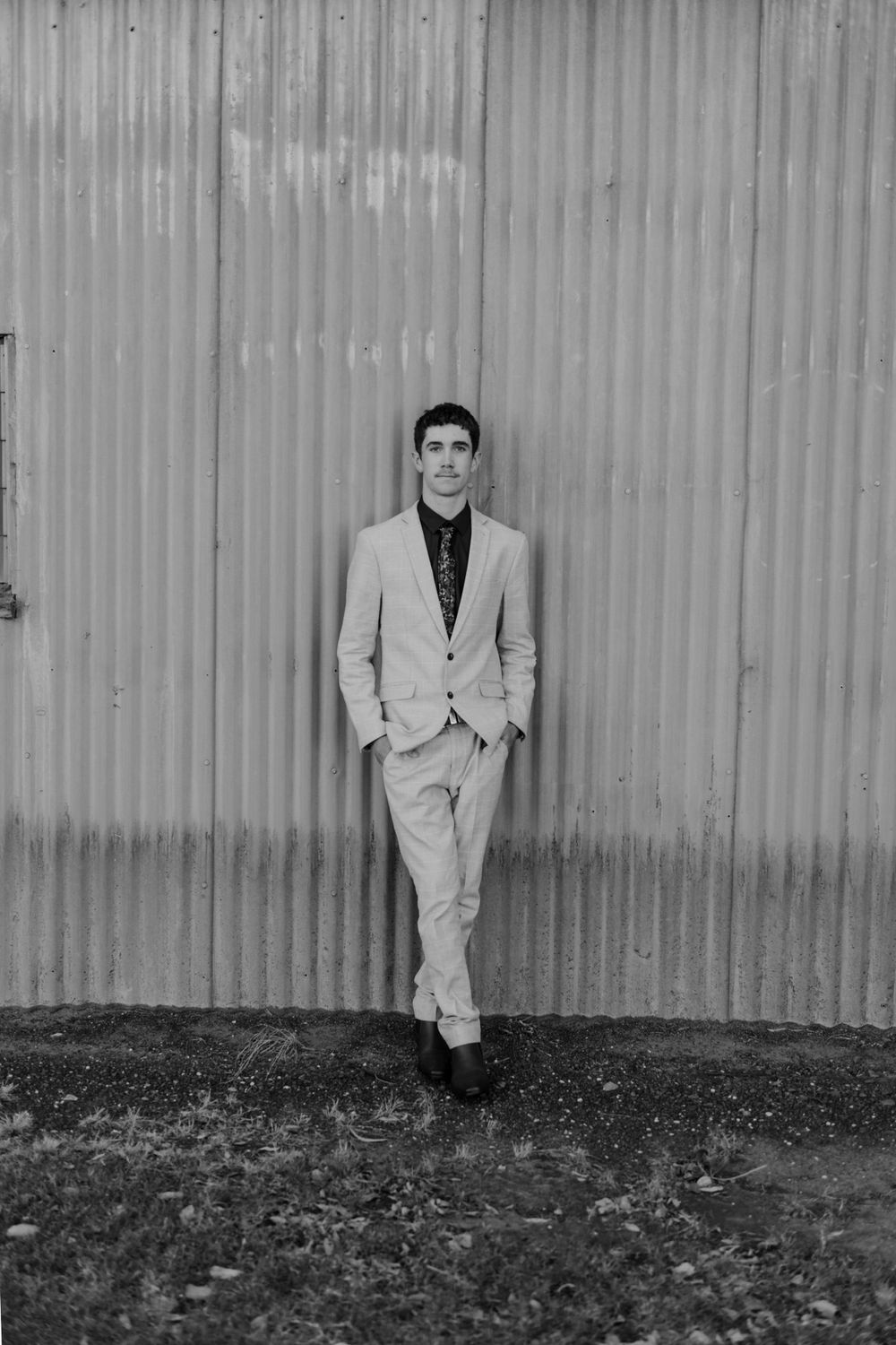 Black and white portrait against corrugated metal wall wearing light suit.