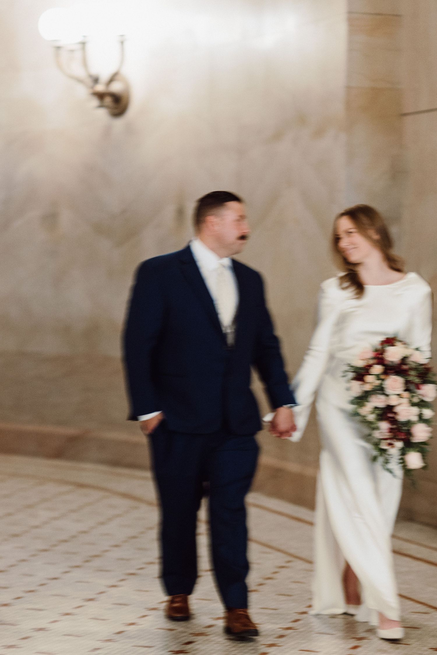 Candid moment of couple walking through elegant hallway with vintage wall decor.