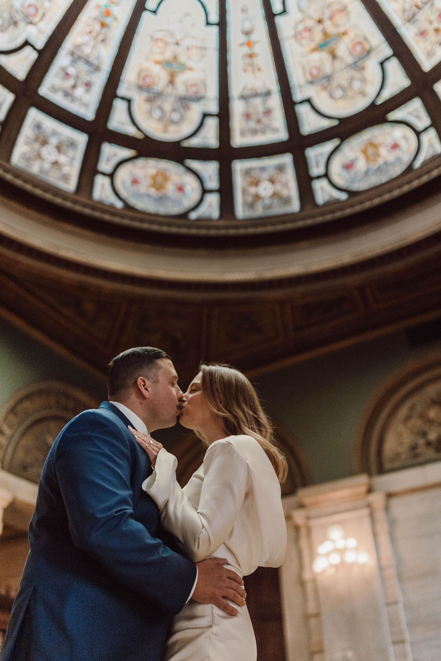 Romantic wedding kiss under beautiful stained glass dome ceiling.