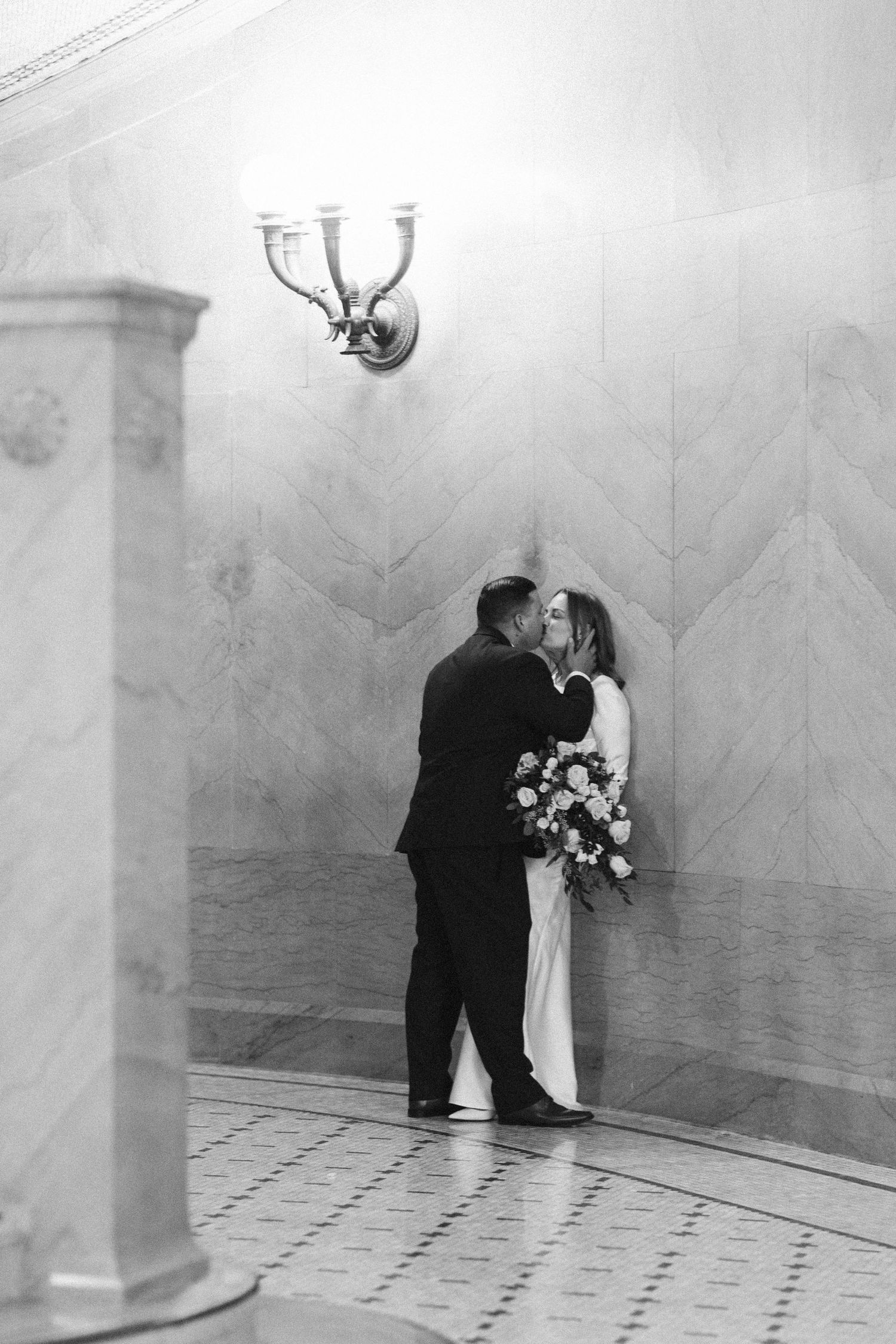 Black and white portrait under vintage wall sconce in elegant hallway.