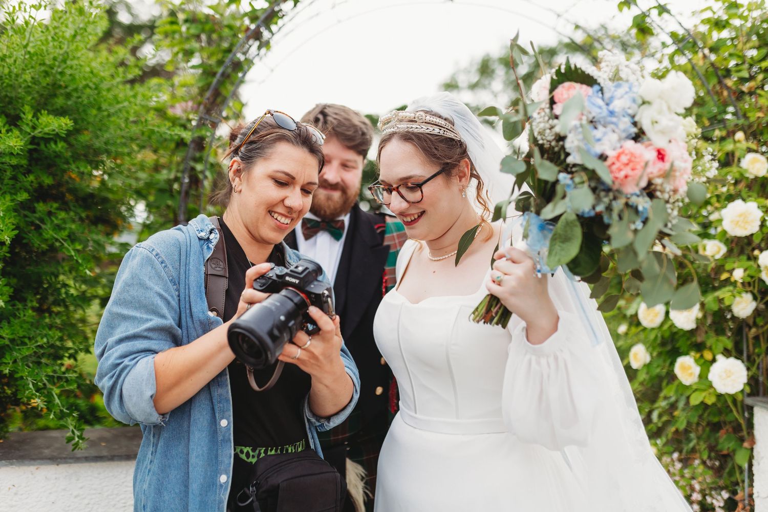 Claire Roige Wedding photographer in blue shirt showing a bride and groom a photo she has taken on her camera while all three smile