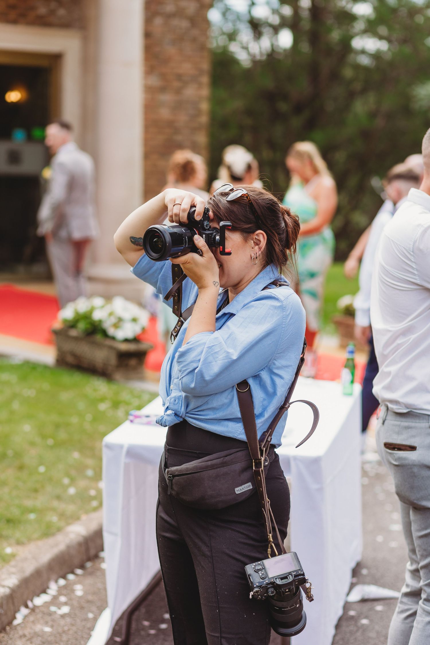 Wedding photographer in blue shirt capturing moments with professional camera equipment.
