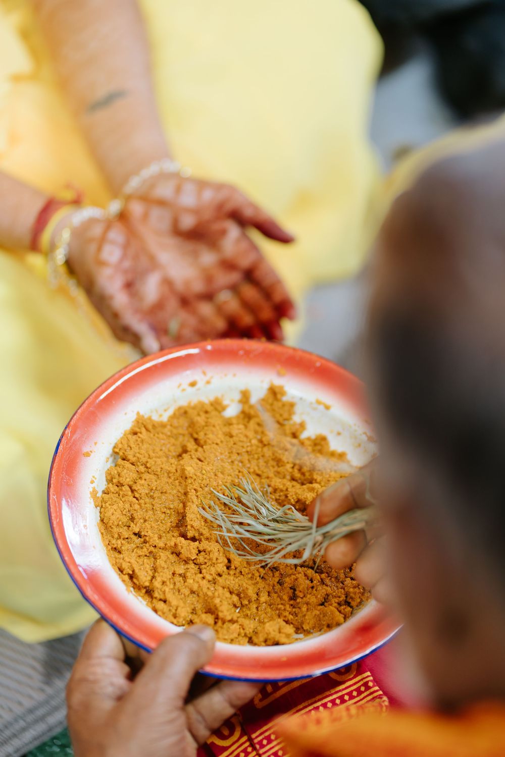 Hands sprinkling aromatic curry powder spices into a bright red bowl in a cooking preparation sequence.