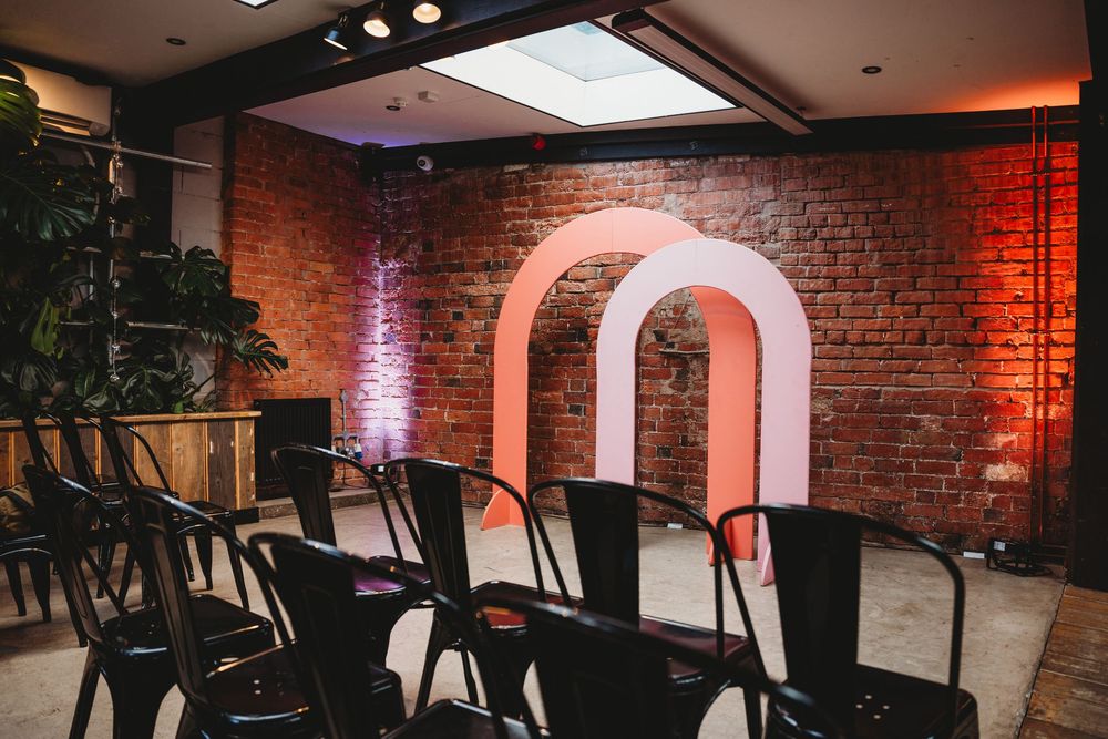 Modern event space with brick walls, arched doorway, and black chairs set up for ceremony.