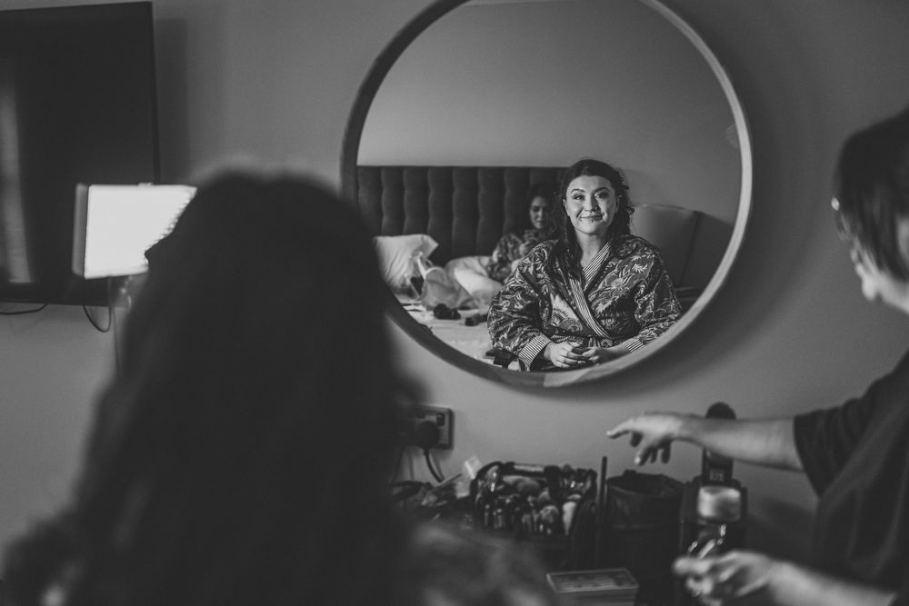 Black and white image showing reflection in round mirror during preparation scene.