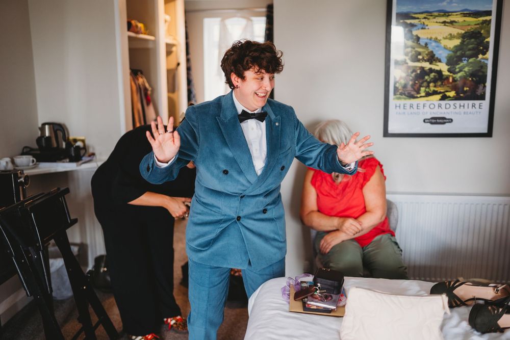 Person in blue suit gestures energetically while others sit nearby during wedding preparations.