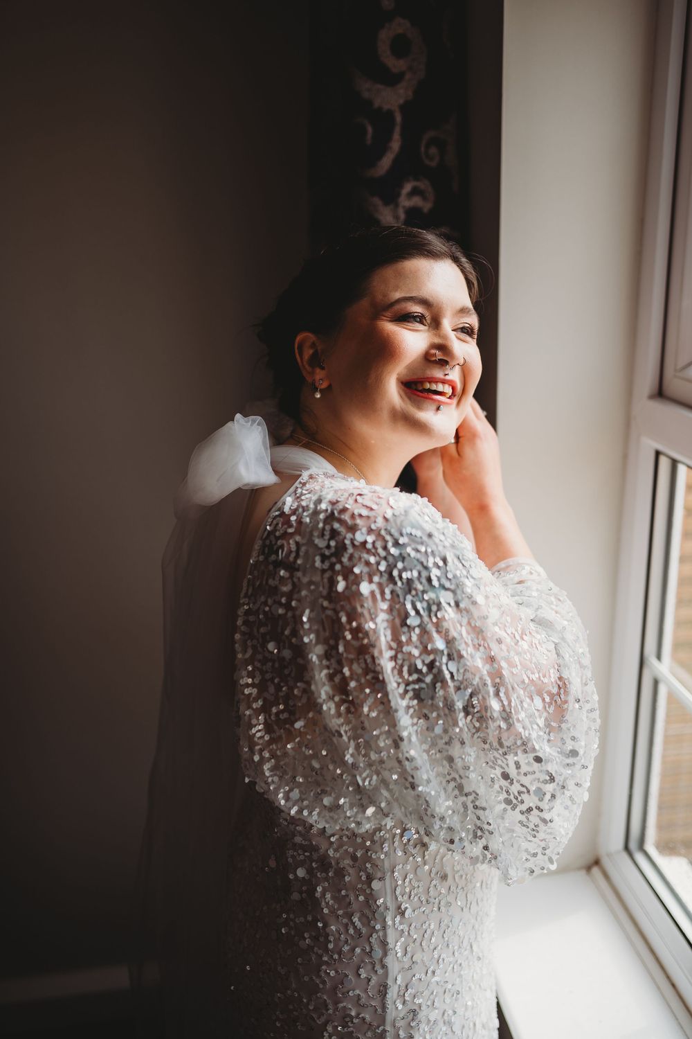 A sparkling beaded wedding dress is showcased near a window in natural light.