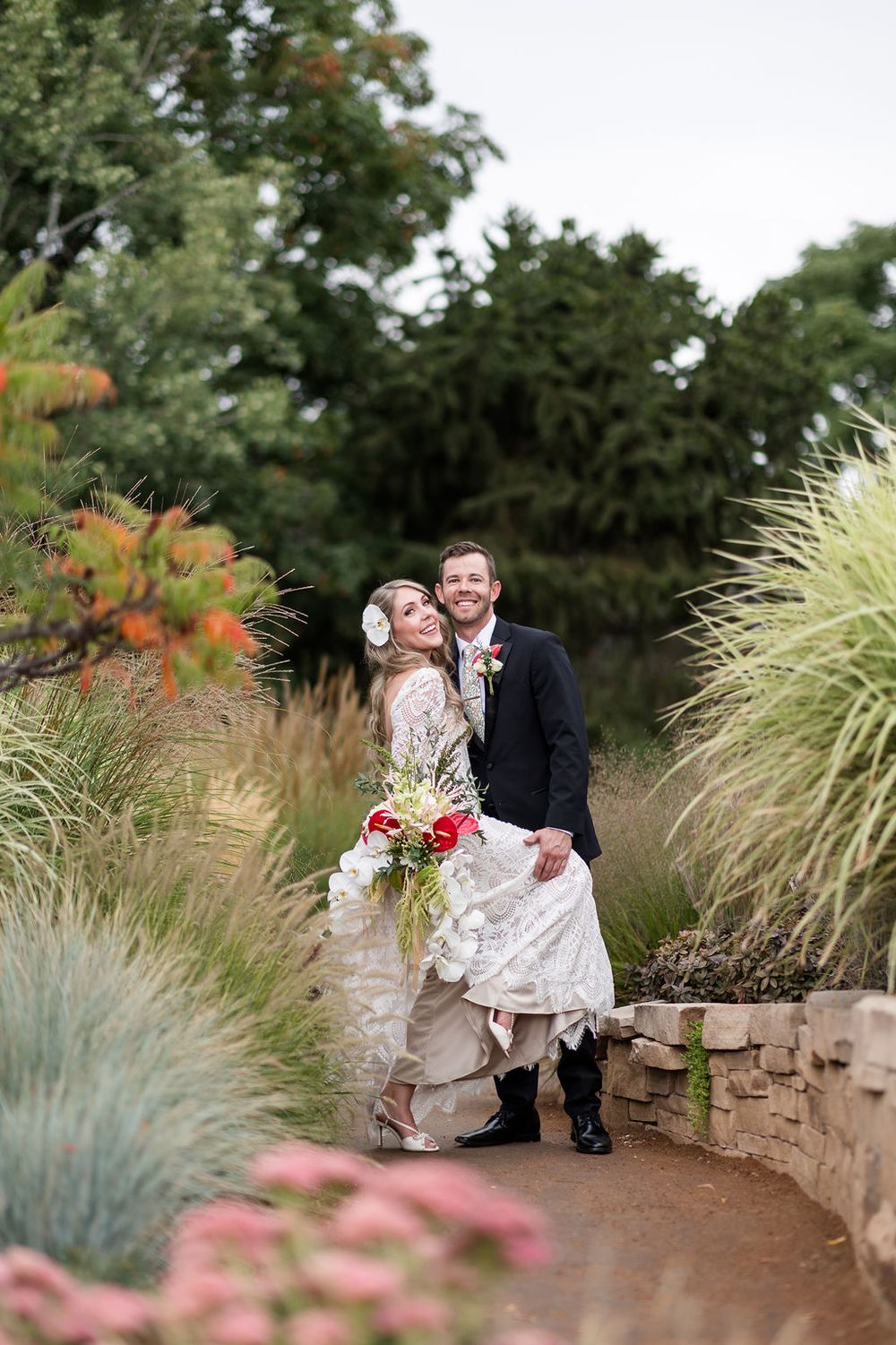 A couple shares a joyful moment on stone steps surrounded by ornamental grasses and garden flowers.
