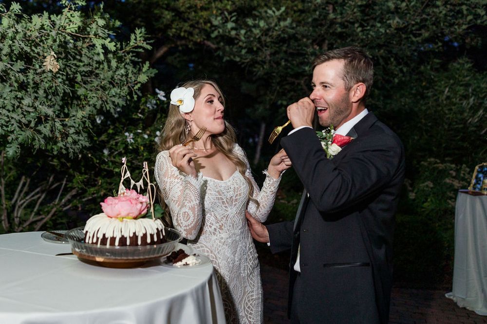 Couple sharing a slice of chocolate drip cake at an outdoor wedding reception.