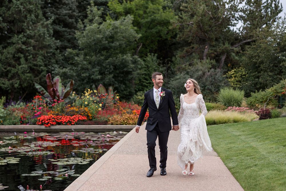 A couple walks through a scenic garden path surrounded by lush greenery and blooming flowers.