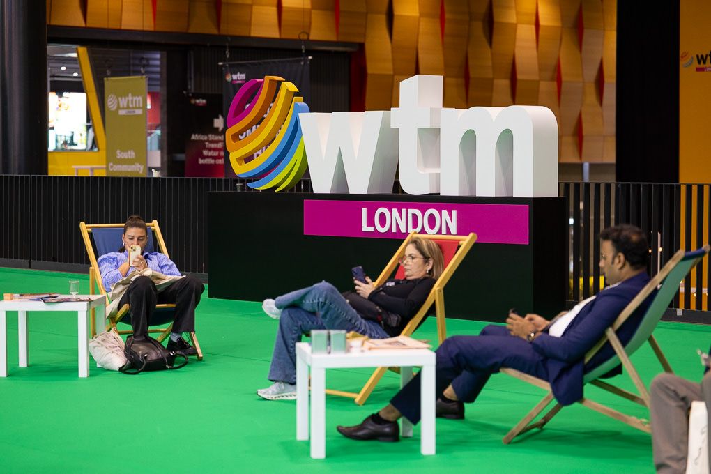 People relax in deck chairs in front of the WTM London logo.