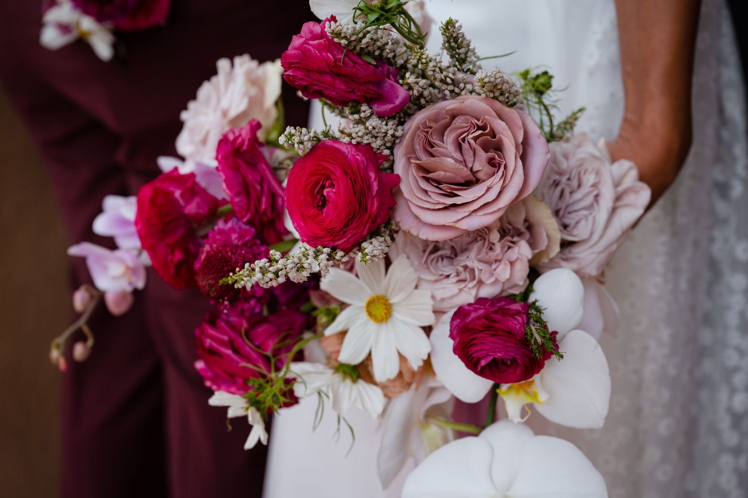 Elegant wedding bouquet featuring deep pink ranunculus, blush roses, and white daisies with delicate greenery accents.