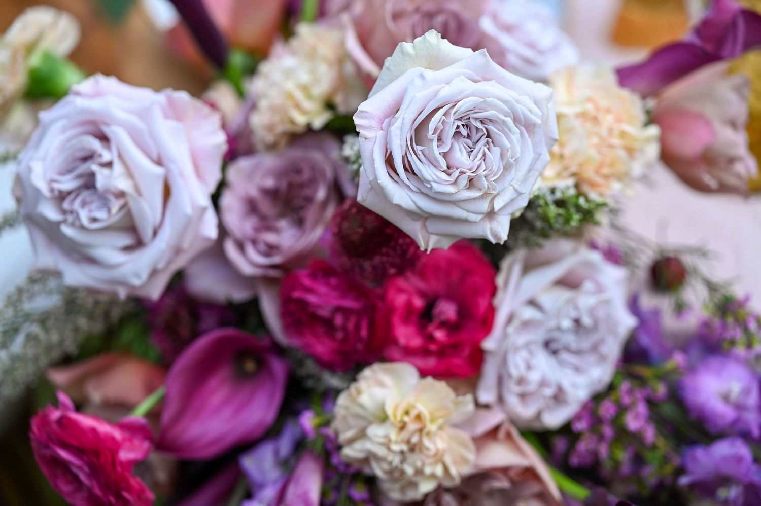 Close-up of a romantic floral arrangement with lavender roses, fuchsia blooms, and carnations in soft focus.