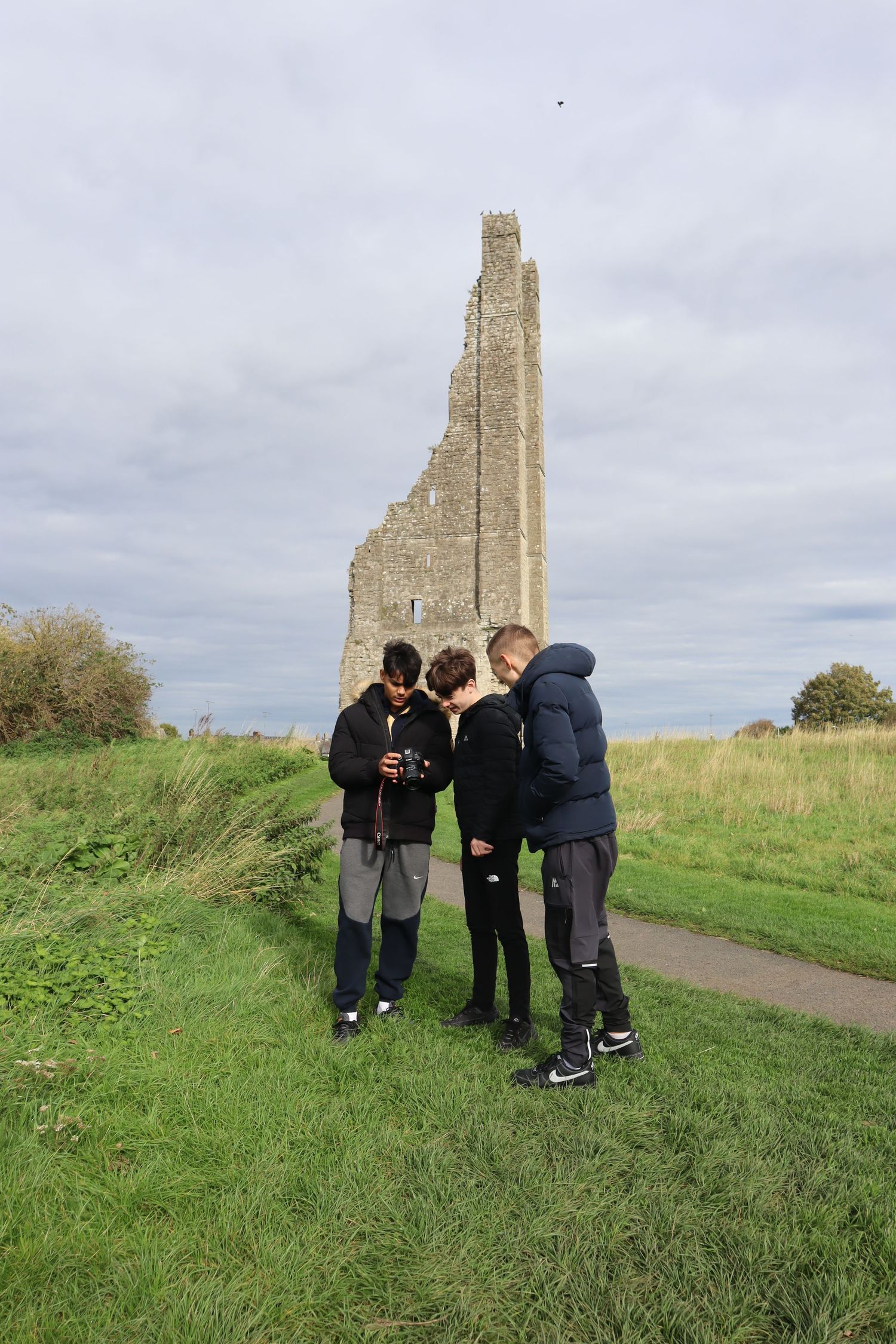 Group examining historic stone ruins on a grassy hillside under cloudy skies.