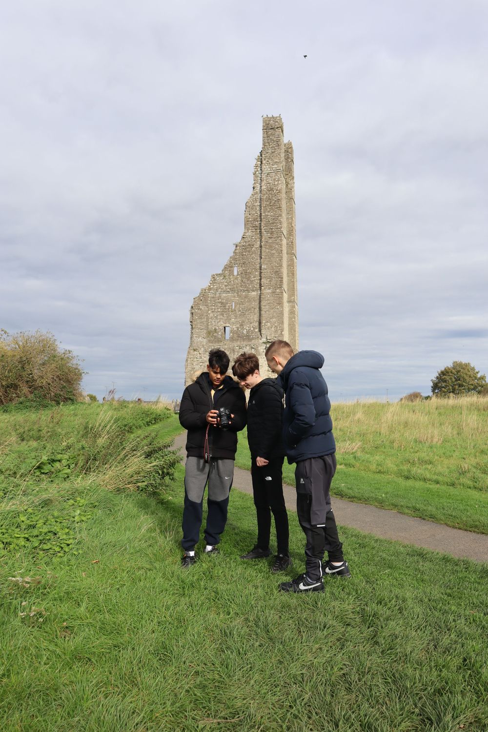Group examining historic stone ruins on a grassy hillside under cloudy skies.