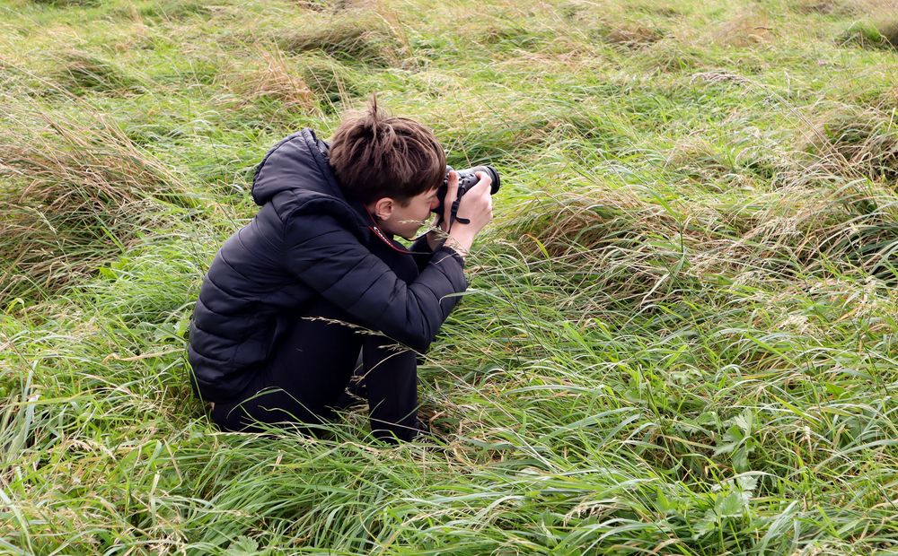 People crouching in tall grass taking nature photographs.