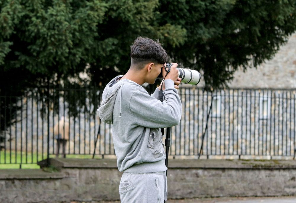 Person taking photographs with a camera in an outdoor setting with trees.