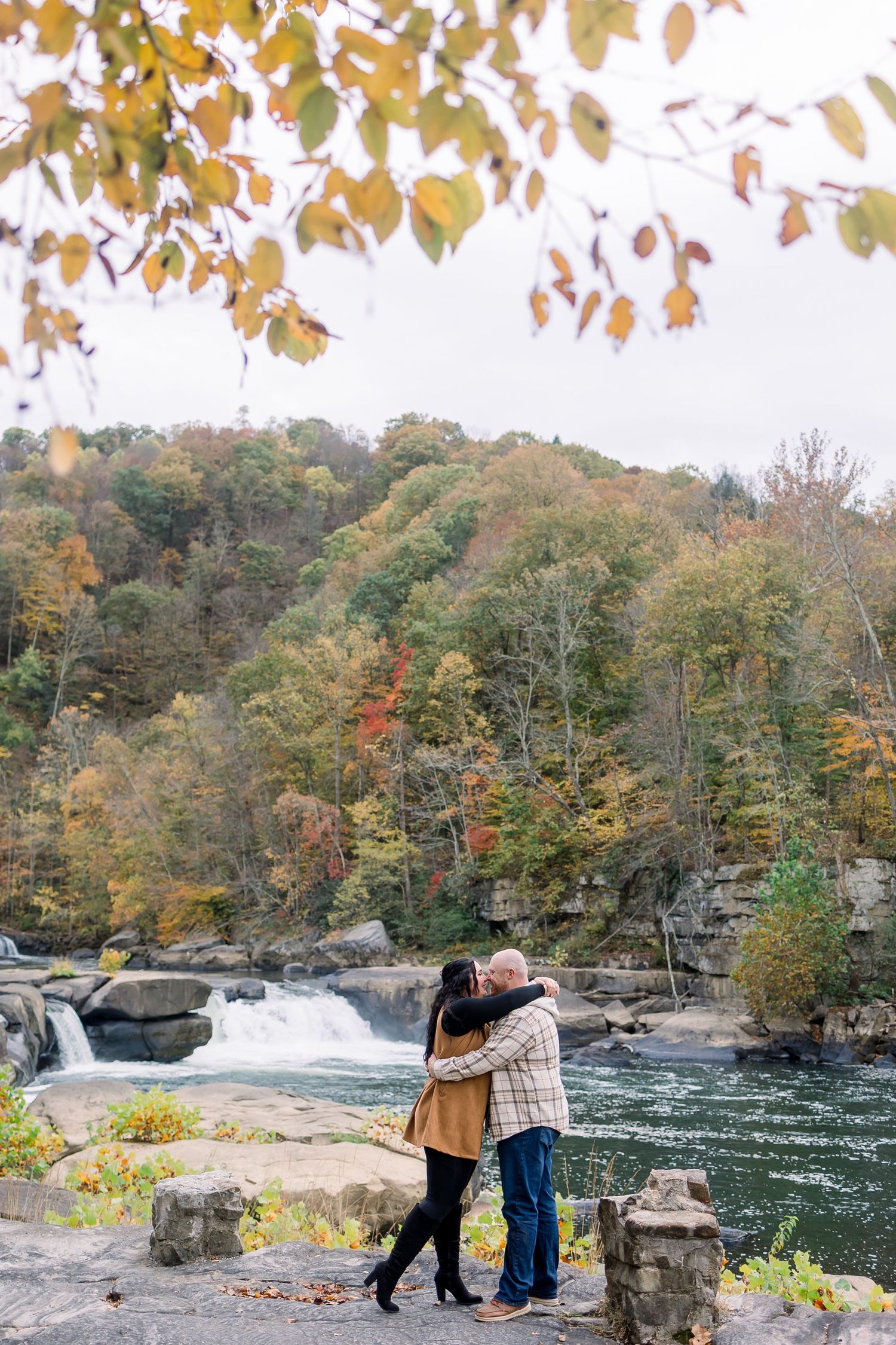 Couple admiring scenic autumn waterfall and river surrounded by colorful fall foliage in a forest landscape.