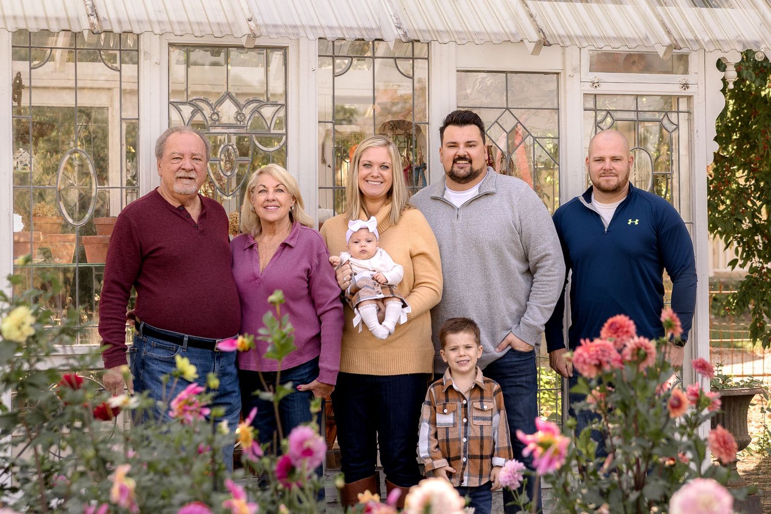 Large family group poses together for outdoor portrait session in front of greenhouse.