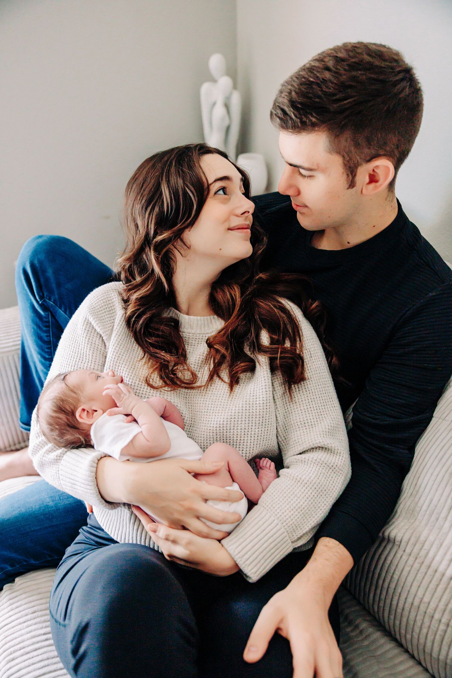 A couple shares tender moments with their newborn baby while sitting on a couch in a series of intimate photos.