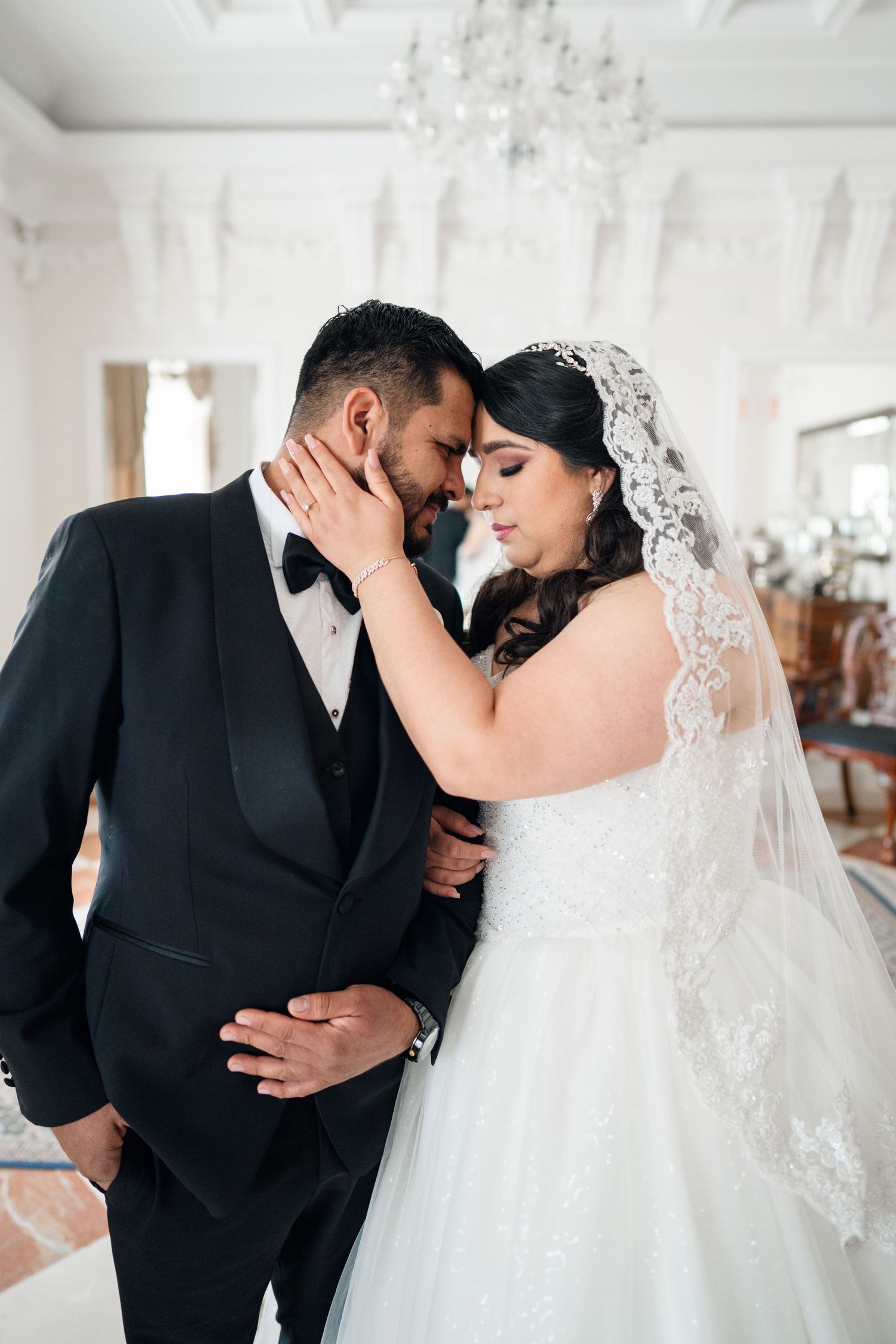 Intimate wedding portraits in an elegant white room with crystal chandelier.